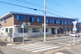 介護施設の建物外観。2階建てのレンガ調ファサード、複数の窓、駐車場を備える。